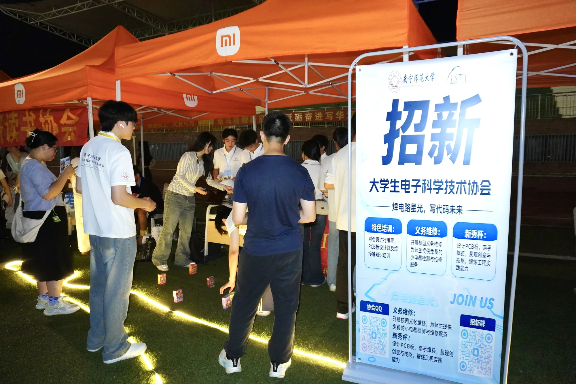 夜间招新摊位，学生在宣传牌前交谈
